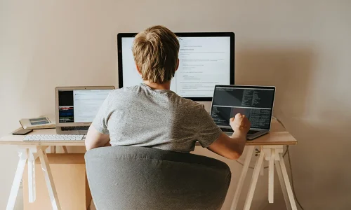 back-view-of-a-boy-sitting-on-grey-chair-while-using-his-laptop-computers